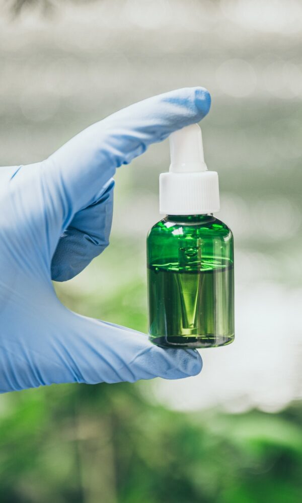 cbd-hemp-oil-hand-holding-bottle-of-cannabis-oil-against-marijuana-plant-6.jpg